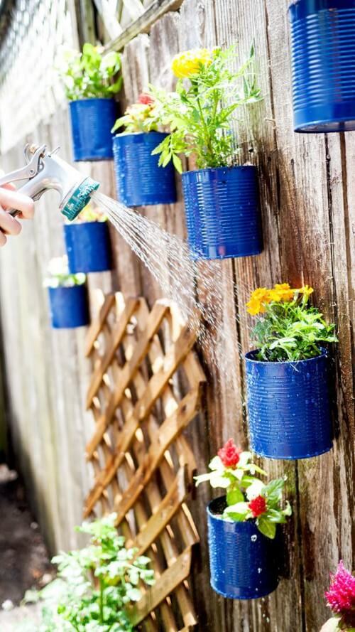 Moça regando horta vertical feita de latas metálicas