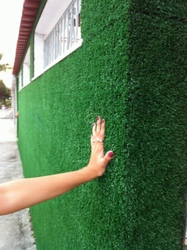 Mão tocando um muro de grama sintética